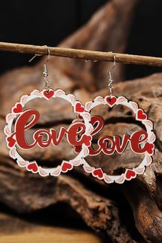 earrings with the word love on them hanging from a wooden stick in front of some wood