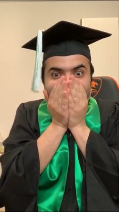 a graduate covers his face with his hands as he stands in front of the camera