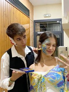 a man and woman with face paint on their faces taking a selfie in front of a mirror