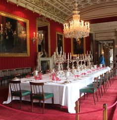 a long table with many candles on it in a room filled with paintings and chandeliers