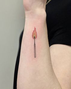 a woman's arm with a small fire stick tattoo on it