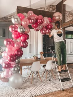 a woman standing on a ladder in front of a table with pink and silver balloons