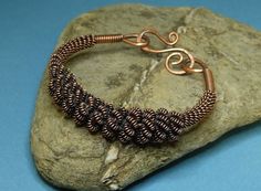 a copper and black wire bracelet sitting on top of a rock