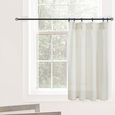 a white curtain hanging from the side of a window in front of a wooden chair