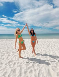 two women in bikinis standing on the beach with their arms up to each other