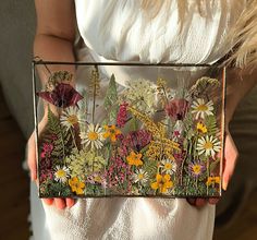 a woman is holding a glass box with flowers on it