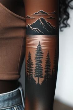 a woman's arm with trees and mountains tattooed on the back of her body