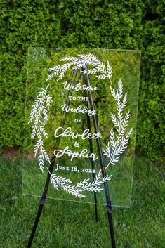 a clear acrylic sign sitting on top of a grass covered field next to a bush