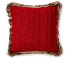 a red pillow with faux fur trim and a cabled design on the front, sitting against a white background