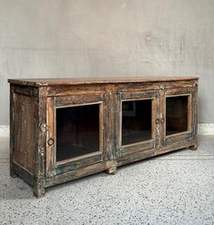 an old wooden sideboard with glass doors on the front and bottom, against a gray wall