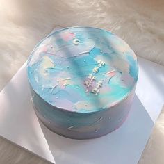 a round cake with blue and pink frosting on top sitting on a white surface