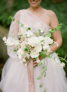 a woman in a wedding dress holding a bridal bouquet with white flowers and greenery