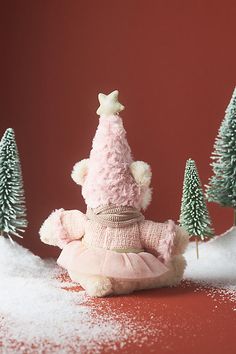 a teddy bear wearing a pink dress sitting in the snow next to some small trees