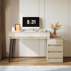 a desk with a computer on top of it next to a vase and flower arrangement