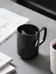 a black coffee mug sitting on top of a table next to a book and pen