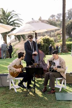 three men playing instruments in the grass under umbrellas at an outdoor event with palm trees and lawn chairs