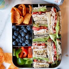 a lunch box filled with sandwiches, fruit and chips