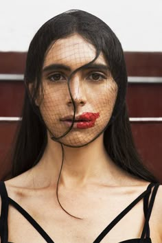 a woman with black hair and red lipstick wearing a veil over her face to cover her eyes