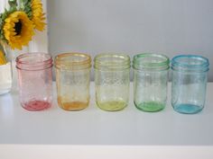 six different colored mason jars lined up on a counter next to a vase with sunflowers