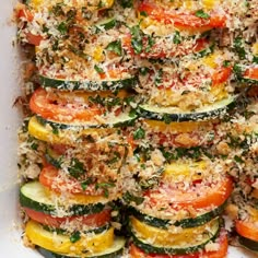 a white dish filled with zucchini and tomatoes covered in parmesan cheese