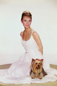 a woman in a white dress sitting on a towel with a dog next to her