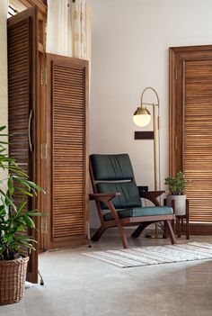 a chair and lamp in a room with wooden shutters on the wall, potted plant next to it