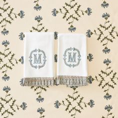 two white towels with monogrammed letters on them sitting on a floral wallpaper