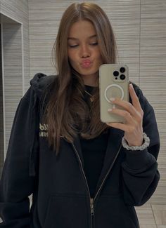 a woman taking a selfie with her phone in front of her face and wearing a black hoodie