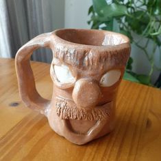 a ceramic mug with a face on it sitting on a table next to a potted plant