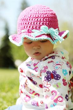 a baby wearing a pink hat sitting in the grass with her hands on her knees