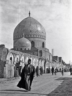 an old black and white photo of a man walking in front of a large building