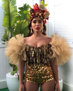 a woman wearing a gold and red outfit with sequins on her head is standing in front of a potted plant