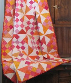 an orange and pink quilt is hanging on a wooden cabinet next to a brown dresser