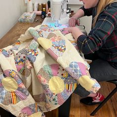 a woman sitting at a table working on a quilt