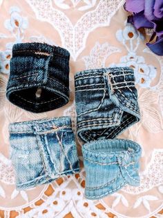 three pairs of jeans sitting on top of a lace doily next to purple flowers