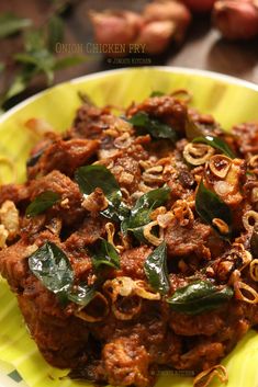 a yellow plate topped with meat covered in sauce and greens on top of it next to onions