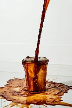 a glass filled with liquid sitting on top of a table next to a white wall