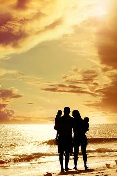 three people are standing on the beach with their arms around each other as the sun sets