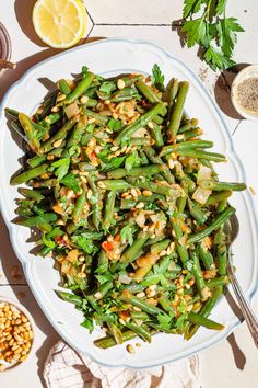 a white plate topped with green beans and other foods next to lemons on a table