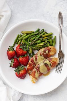 a white plate topped with chicken, asparagus and strawberries