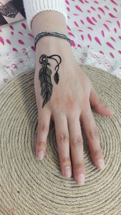 a woman's hand with a small black feather tattoo on her left arm and wrist