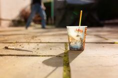 a cup with a straw in it sitting on the ground next to a person walking