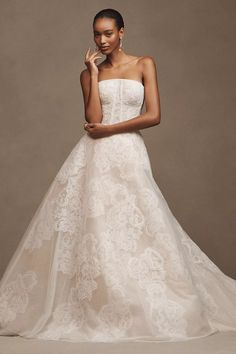 a woman in a strapless wedding dress poses with her hand on her chin and looking at the camera