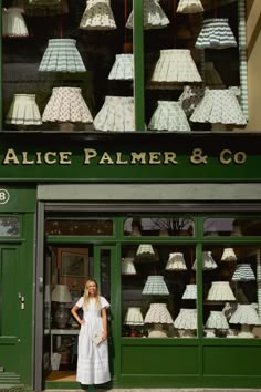 a woman standing in front of a green storefront with lamps hanging from it's windows