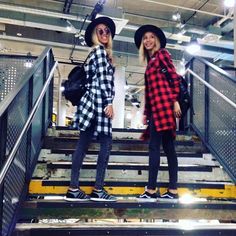 two young women standing on the stairs in front of an escalator wearing plaid shirts and hats