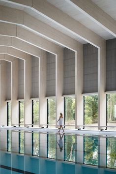 a woman is walking in front of a swimming pool with large windows on both sides