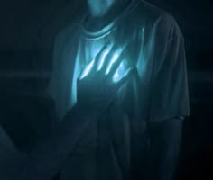 a man holding his hands up in the dark with glowing light on it's chest