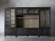 a black entertainment center with glass doors and drawers on the side, in front of a concrete wall