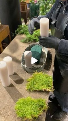 a man in black jacket sitting at a table with candles and moss growing on it