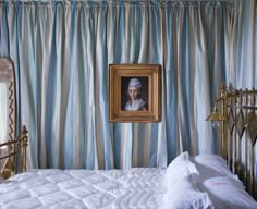 a painting hangs on the wall next to a bed with white sheets and blue drapes